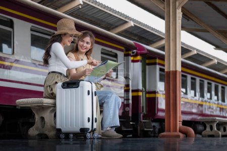Foto de Concepto de viaje. amiga usar sombrero que sostiene mapa tienen bolsa y equipaje. mujer viajera esperando tren en la estación de tren. - Imagen libre de derechos