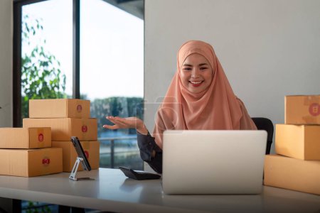 Photo for Muslim women selling online at home with box. Selling online with box to accept order from customer. SME business idea. Parcel delivery. muslim woman working smartphone and laptop at home. - Royalty Free Image