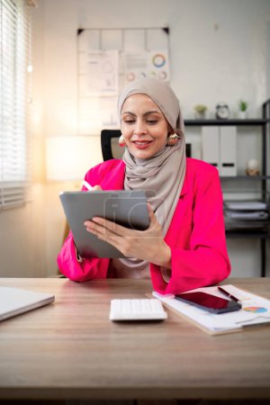 Foto de Joven mujer musulmana de negocios hijab feliz usando tableta digital en la oficina moderna. - Imagen libre de derechos