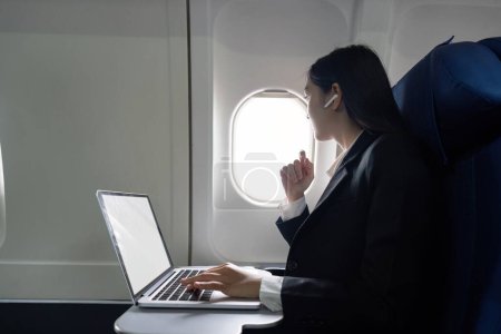Photo for Successful young asian business woman sits in airplane cabin plane and working from anywhere. Flying at first class. - Royalty Free Image