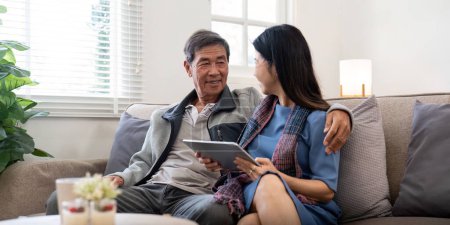 Foto de Feliz anciano asiático pareja usando tableta sentarse en sofá haciendo ecommerce compras en línea en el sitio web y la compra de seguro de navegación en casa. - Imagen libre de derechos