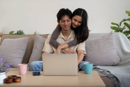 Téléchargez les photos : Heureux couple asiatique asseoir relax sur canapé dans salon regarder vidéo sur portable ensemble à la maison. - en image libre de droit