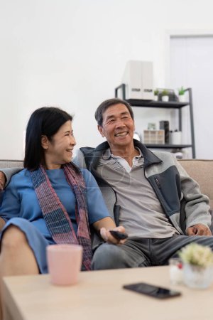 Téléchargez les photos : Asiatique couple aîné profiter de leur télévision préférée. Joyeux couple de retraités regardant la télévision ensemble dans le salon. - en image libre de droit