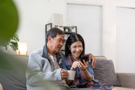 Foto de Retrato de asiático adorable pareja de personas mayores utilizando el teléfono inteligente juntos video chat con la familia en la sala de estar en casa.. - Imagen libre de derechos