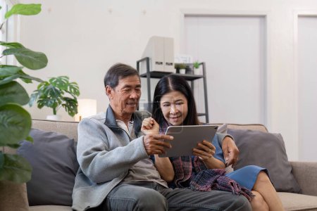 Téléchargez les photos : Heureux couple de personnes âgées asiatiques utilisant tablette numérique ensemble sur canapé intérieur dans le salon. Bonne retraite activité mode de vie à la maison.. - en image libre de droit
