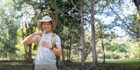 Téléchargez les photos : Voyageur randonneur homme portant un sac à dos sur le dos et la marche dans le parc national. homme asiatique est repos par boisson eau. - en image libre de droit
