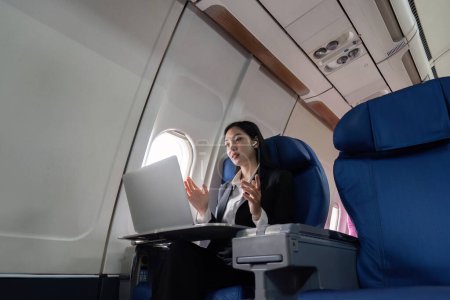 Photo for Successful young asian business woman sits in airplane cabin plane and working from anywhere. Flying at first class. - Royalty Free Image
