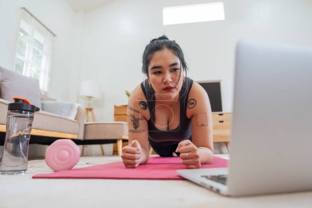 Téléchargez les photos : Asiatique femme en surpoids faisant des exercices d'étirement à la maison sur la forme physique, cours de conditionnement physique en ligne. Entraînement d'étirement sur tapis de yoga à la maison pour une bonne santé et forme du corps. - en image libre de droit