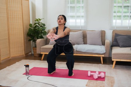 Photo for Overweight woman enjoying a fitness workout at home. Fat, plump woman and squatting on an exercise mat in the living room. - Royalty Free Image