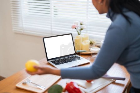 Téléchargez les photos : Joyeux gros femme cuisine dans la cuisine montrant ordinateur portable maquette écran blanc vierge à la maison. - en image libre de droit