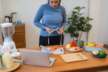 Foto de Mujer joven asiática medir su cintura en la cocina el con verduras y frutas. Concepto de alimentación saludable y dieta. - Imagen libre de derechos