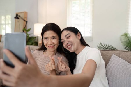 Photo for Daughter adult taking selfie using mobile phone with senior mother at home. - Royalty Free Image