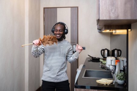 Téléchargez les photos : Afro-Américain écouter de la musique tout en nettoyant dans la cuisine. - en image libre de droit