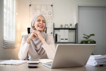 Téléchargez les photos : Femme d'affaires musulmane hijab travailler sur la finance avec rapport d'entreprise et calculatrice sur ordinateur portable dans le bureau à domicile. - en image libre de droit