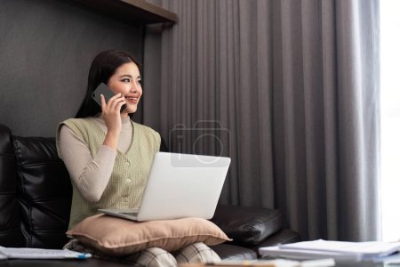 Photo for Happy young asian freelance business woman sitting on the floor at home working on digital tablet while drinking coffee and talk on the phone. - Royalty Free Image