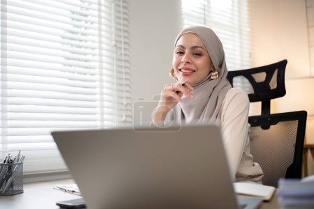 Téléchargez les photos : Femme d'affaires musulmane asiatique en hijab foulard travailler avec document papier dans le bureau moderne. diversité et concept de bureau. - en image libre de droit