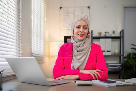 Foto de Mujer musulmana de negocios hijab trabajando sobre finanzas con informe de negocios y calculadora en la computadora portátil en la oficina en el hogar. - Imagen libre de derechos
