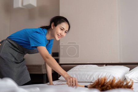 Téléchargez les photos : Une femme asiatique service de nettoyage du personnel, outil et seau pour le travail. une jeune femme nettoyeuse avec des produits pour nettoyer une chambre, Dust off the bed. - en image libre de droit
