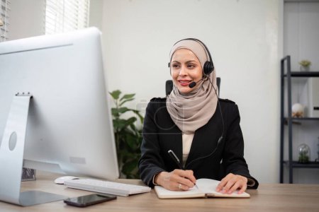 Foto de Mujeres musulmanas jóvenes que usan telemarketing hijab o agente de centro de llamadas con auriculares que trabajan en la línea directa de apoyo en la oficina. - Imagen libre de derechos