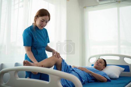 Foto de Fisioterapeuta mujer asiática, haciendo fisioterapia de piernas para el hombre de edad avanzada para tratar la osteoartritis y el dolor nervioso en la pierna a la enfermería en el hogar y el concepto de atención médica. - Imagen libre de derechos