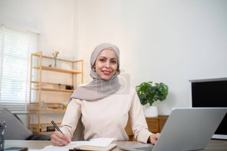 Foto de Joven mujer musulmana contable de negocios que trabaja con facturas de documentos financieros, calcular impuestos. Mujer musulmana freelancer papeleo en casa. - Imagen libre de derechos