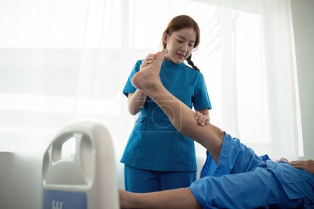 Téléchargez les photos : Physiothérapeute femme asiatique, faire de la physiothérapie des jambes pour les hommes âgés pour traiter l'arthrose et les douleurs nerveuses dans la jambe aux soins infirmiers à domicile et concept de soins de santé. - en image libre de droit