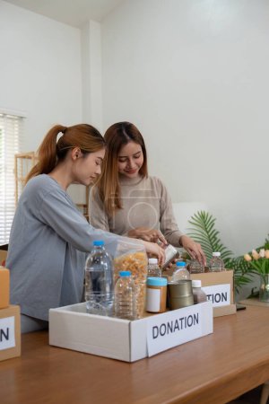 Téléchargez les photos : Don et deux femmes bénévoles asiatiques heureux emballage des aliments dans la boîte à la maison. Organisme de bienfaisance. - en image libre de droit