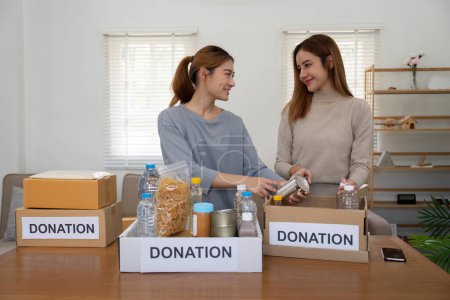 Téléchargez les photos : Heureuse jeune femme bénévole collectant, triant la nourriture pour les personnes nécessiteuses, équipe travaillant ensemble sur un projet de don dans la charité à la maison. - en image libre de droit