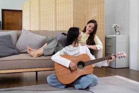 Foto de Asiático joven amante lesbiana pareja jugando guitarra con relajarse y feliz momento en sala de estar LGBT relación en el concepto de estilo de vida. - Imagen libre de derechos