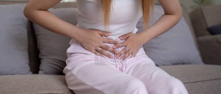 Photo for Young woman suffering from stomach ache on sofa at home. - Royalty Free Image