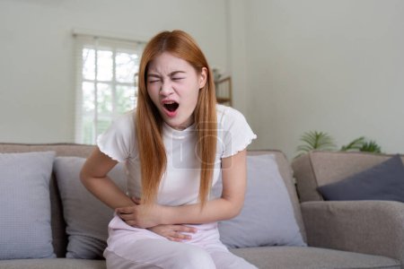 Foto de Mujer asiática que sufre de dolor de estómago en casa, Mujer que sufre de dolor abdominal. - Imagen libre de derechos