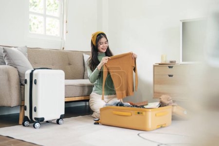 Téléchargez les photos : Joyeux asiatique jeune femme valise d'emballage à la maison. Se préparer pour les vacances d'été à l'étranger Voyage.. - en image libre de droit