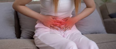 Photo for Young woman suffering from stomach ache on sofa at home. - Royalty Free Image