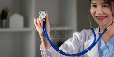 Photo for Smiling asian female doctor holding stethoscope, healthcare professional in clinic. - Royalty Free Image