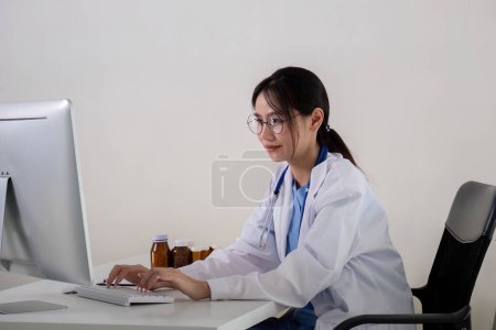Asian Female Doctor Working on Computer in Medical Office.