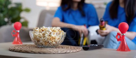 Photo for Lesbian couple cheering for Euro football at home with popcorn and air horn. Concept of LGBTQ pride, celebration, and sports excitement. - Royalty Free Image
