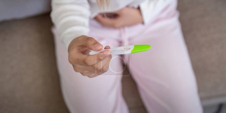 Test de grossesse positif tenu par la femme à la maison, montrant le bonheur. Concept de nouveaux débuts et de découverte joyeuse.