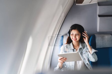 Hipster-Reisende mit Tablet und Kopfhörer im Flugzeug während der Sommerferien. Unterhaltung und Entspannung im Flug genießen.