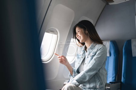 Hipster traveler enjoying airplane view during summer vacation. Happy woman pointing out airplane window in casual attire.