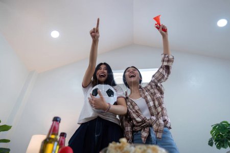 Asian friends cheering while watching Euro football match at home. Concept cheer and excitement.