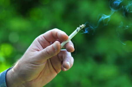 Téléchargez les photos : Fumeur tient un allumé sur cigarette dans sa main, à l'extérieur de l'espace de bureau - en image libre de droit