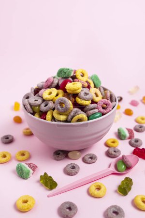 Photo for A bowl of cereal and candies with a pink spoon on a pink background - Royalty Free Image