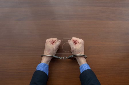 Photo for Top view, handcuffed hands of an arrested criminal on the table of the police station. copy space - Royalty Free Image