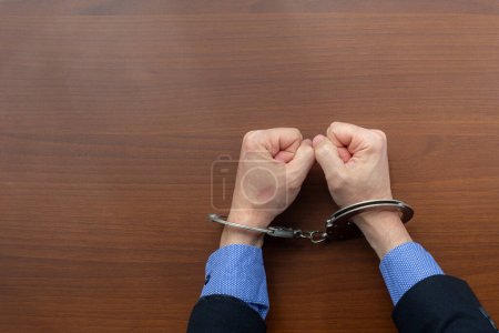 Draufsicht, gefesselte Hände eines festgenommenen Verbrechers auf dem Tisch der Polizeiwache. Kopierraum