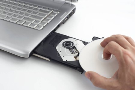 Photo for Hand inserts dvd disc into laptop, concept of burning data to dvd on isolating background - Royalty Free Image