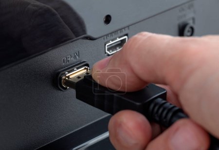 Primer plano de una mano conectando un cable DisplayPort al conector DP-IN. Inserte el cable DisplayPort