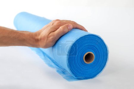 Téléchargez les photos : Une main déroule un rouleau de tissu bleu, un drap pour massage, sur un fond blanc. - en image libre de droit