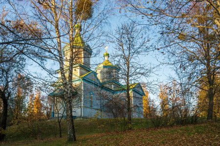 Historical Wooden Church of Saint Paraskeva Friday in Pereiaslav, Ukraine. The church is surrounded by trees with autumn foliage. The sky is blue and the sun is shining.