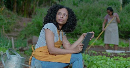 Photo for A pensive black woman at urban farm holding tablet. Thoughtful African American female person at local small business farm - Royalty Free Image