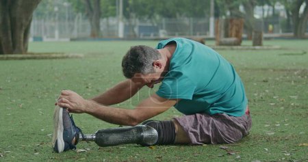 Téléchargez les photos : Un athlète handicapé d'âge moyen âgé motivé étirant une jambe prothétique - en image libre de droit